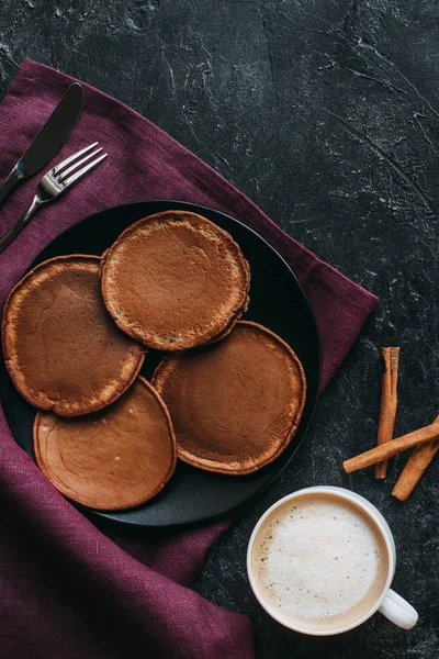 Top view of chocolate pancakes and cup of coffee on black concrete surface — Stock Photo