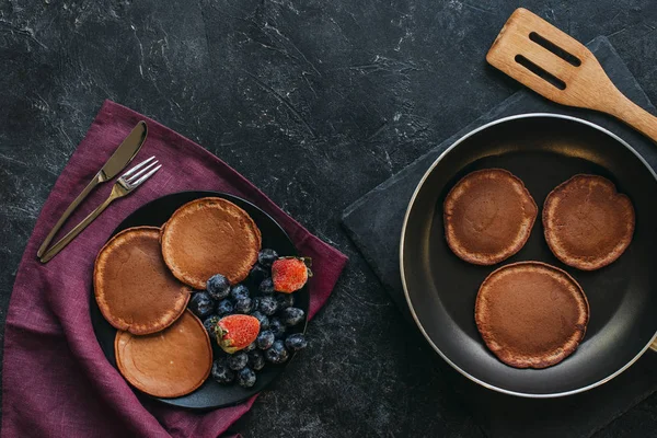 Top view of fresh pancakes on plate and frying pan on black tabletop — Stock Photo