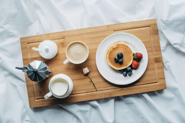 Vista superior do café da manhã na cama com panquecas recém-assadas e café na bandeja de madeira — Fotografia de Stock
