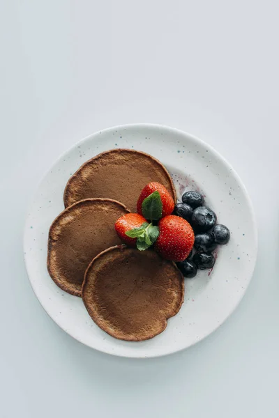 Top view of chocolate pancakes with berries on white table — Stock Photo