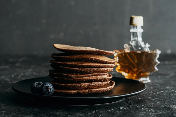 Gestapelte Schokoladen-Pfannkuchen mit einer Flasche Ahornsirup — Stockfoto