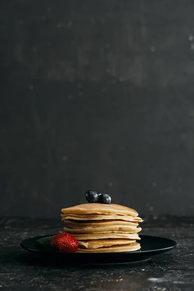 Plato de deliciosos panqueques con bayas en la superficie de hormigón negro - foto de stock