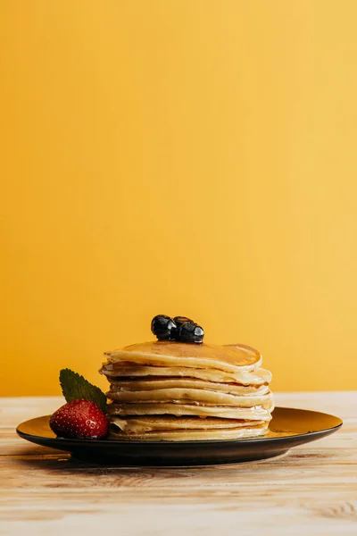 Pila de deliciosos panqueques con bayas en amarillo - foto de stock