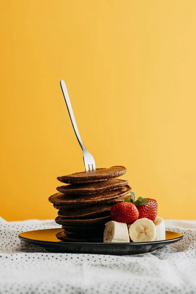 Delicious stacked pancakes pierced with fork on plate with fruits — Stock Photo