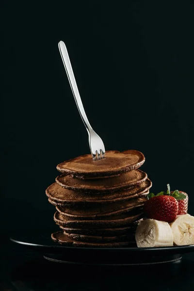 Delicious stacked pancakes pierced with fork on black — Stock Photo