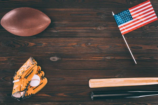 Vista superior de nós bandeira, bola de rugby, bastões de beisebol e luva com bola na mesa de madeira — Fotografia de Stock