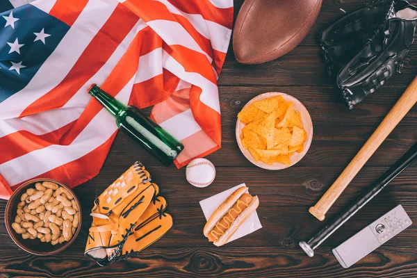 Vista superior de junk food, bandeira americana e equipamentos esportivos na mesa de madeira — Fotografia de Stock