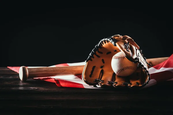 Close-up view of baseball glove with ball and bat on wooden table and us flag on black — Stock Photo