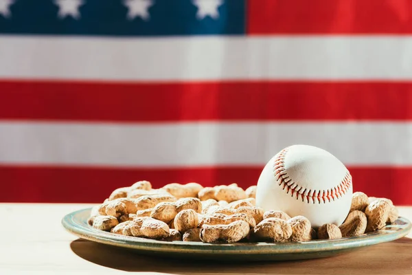 Крупным планом бейсбольный мяч на тарелке с арахисом и американским флагом позади — стоковое фото