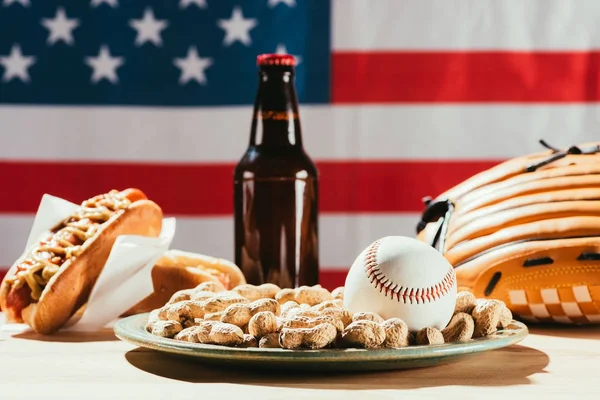 Vista ravvicinata della palla da baseball sul piatto con arachidi e bottiglia di birra con hot dog dietro — Foto stock