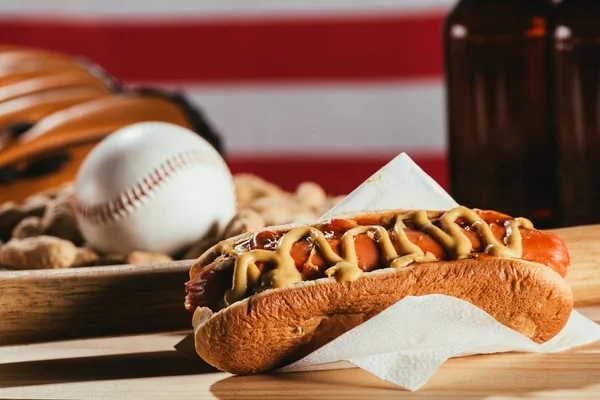 Крупный план хот-дога, бейсбольной биты и спортивного инвентаря на деревянном столе — стоковое фото