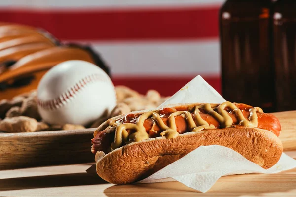 Close-up view of hot dog, baseball bat and sport equipment on wooden table — Stock Photo