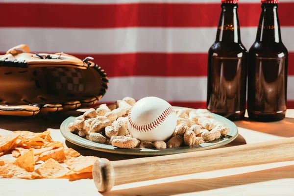 Vue rapprochée de la balle de baseball sur plaque avec cacahuètes, bouteilles de chauve-souris et de bière, gant en cuir et drapeau américain — Photo de stock