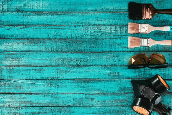 Top view of arranged paint brushes, goggles and protective mask for redecoration on blue wooden surface — Stock Photo