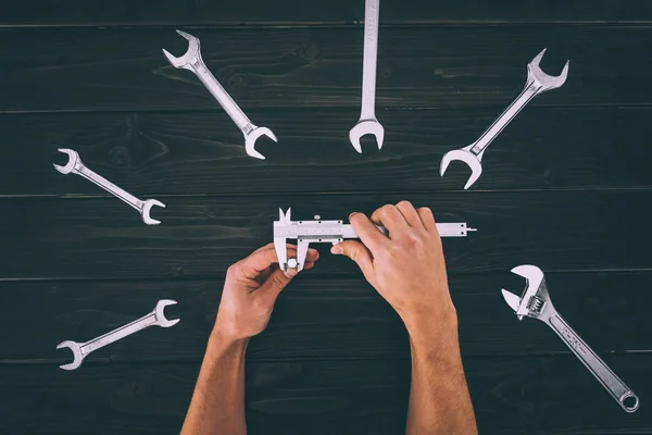 Cropped shot of worker getting measurements with vernier caliper and wrenches on wooden tabletop — Stock Photo