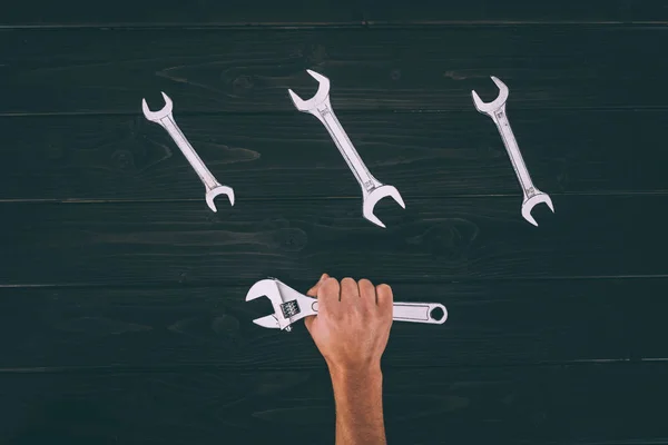 Partial view of male hand holding wrench on wooden surface — Stock Photo