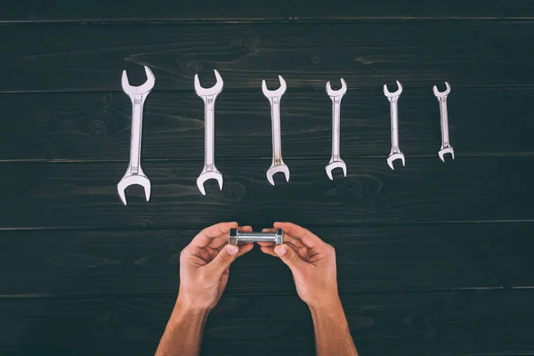 Partial view of worker holding carpentry supply with wrenches around on wooden surface — Stock Photo