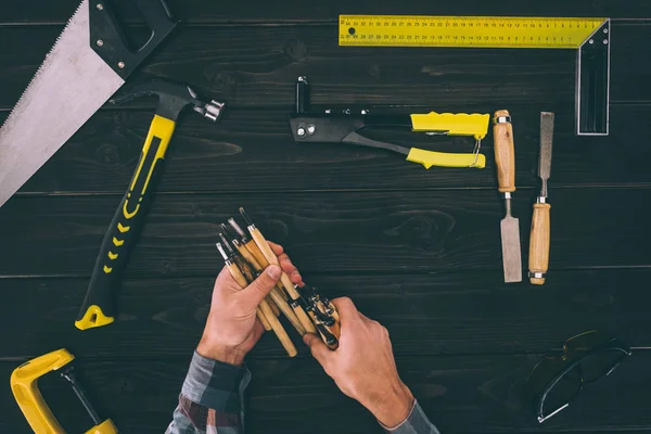 Partial view of carpenter holding chisels with various industrial tools around on wooden tabletop — Stock Photo