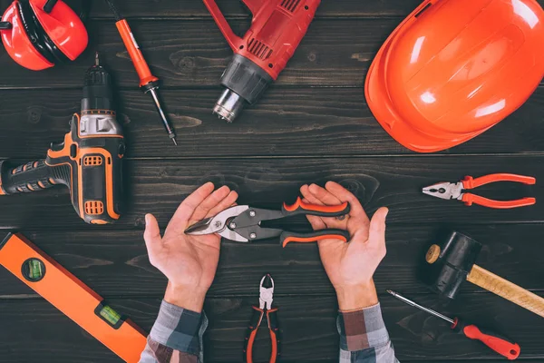 Teilansicht des Arbeiters, der eine Zange mit verschiedenen Vorräten auf einer Holzoberfläche herumhält — Stockfoto