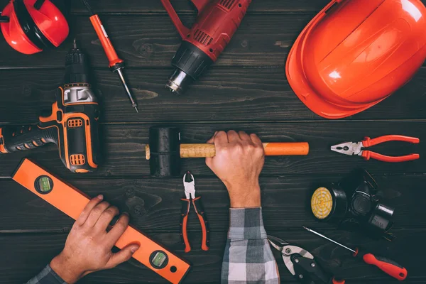 Partial view of worker holding spirit level and hammer with various supplies around on wooden surface — Stock Photo