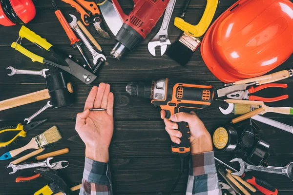 Cropped shot of worker holding electric screwdriver and various supplies on wooden tabletop — Stock Photo