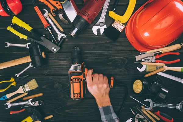 Cropped shot of worker holding electric screwdriver and various supplies on wooden tabletop — Stock Photo