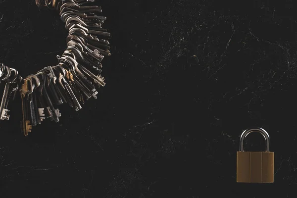 Top view of heap different metal keys with lock on black table — Stock Photo