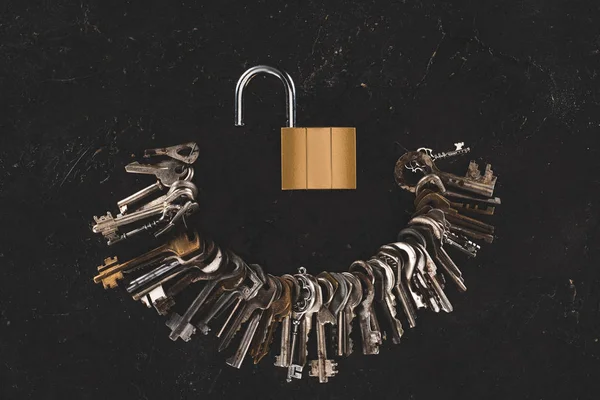 Top view of heap different metal keys with opened lock on black table — Stock Photo