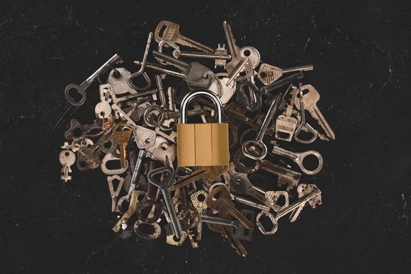 Top view of heap different metal keys with lock on black table — Stock Photo