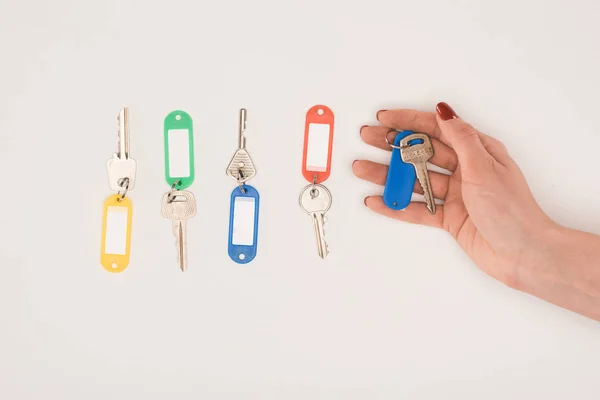 Вид зверху руки тримає ключ поруч з набором ключів з різнокольоровими етикетками ізольовані на білому — стокове фото