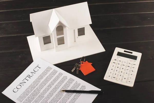 Концепция покупки дома с контрактом, ключами, калькулятором и макетом над деревянным столом — стоковое фото
