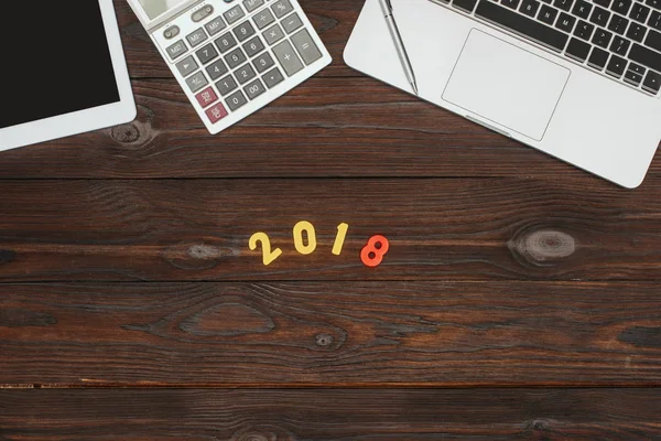 Top view of laptop, tablet, calculator and 2018 numbers on wooden tabletop — Stock Photo