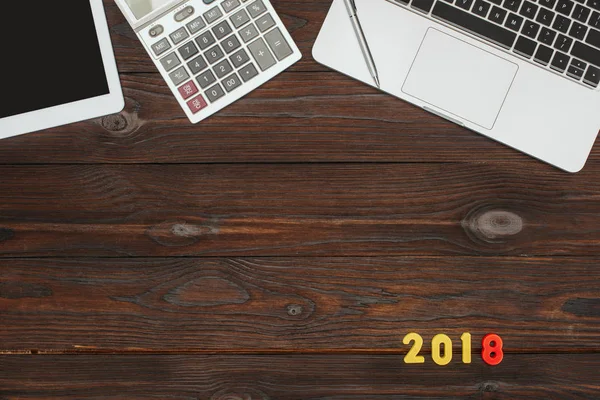 Top view of laptop, tablet, calculator and 2018 numbers on wooden tabletop — Stock Photo