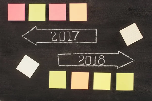 Top view of arranged empty sticky notes and arrows with 2017, 2018 year signs on dark wooden surface — Stock Photo