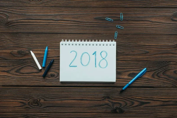 Draufsicht auf arrangiertes Notizbuch mit 2018, Bleistiften, Clips und Stift auf Holztischplatte — Stockfoto