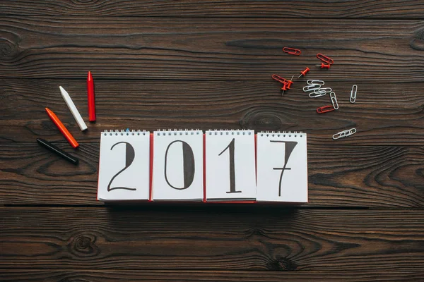 Tendido plano con arreglo de calendario 2018, lápices, alfileres y clips en la mesa de madera oscura - foto de stock