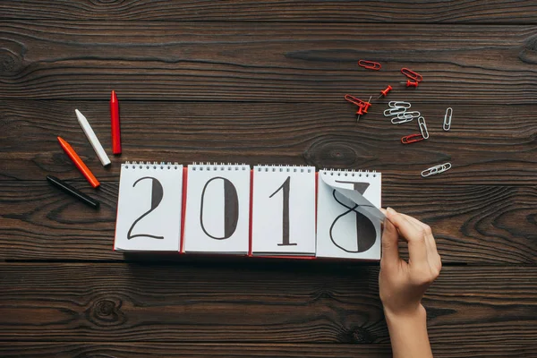 Ritagliato colpo di donna strappando parte del calendario 2018 anno con superficie di legno scuro come sfondo — Foto stock