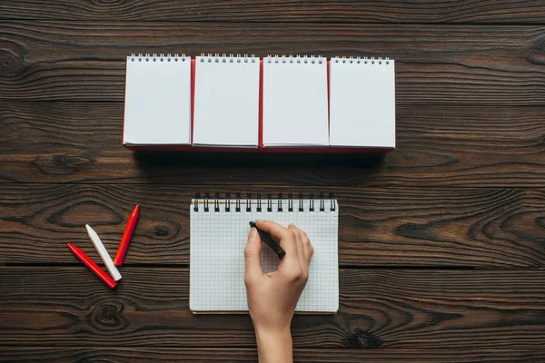 Vue partielle de la femme avec un crayon à la main écrit dans un cahier sur une table en bois — Photo de stock