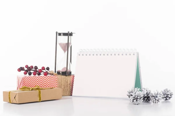 Vista de cerca del calendario en blanco, reloj de arena, conos de pino y regalos envueltos aislados en blanco - foto de stock