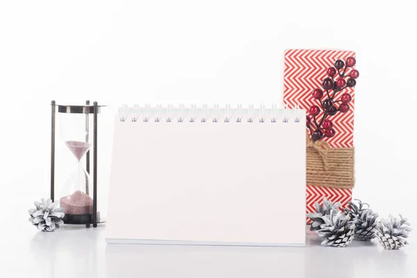 Vista de cerca del calendario en blanco, reloj de arena, conos de pino y regalo envuelto aislado en blanco - foto de stock