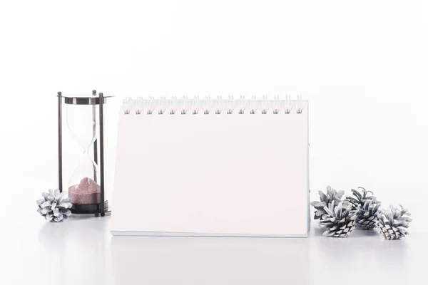 Vista de cerca del calendario en blanco, reloj de arena y conos de pino aislados en blanco - foto de stock