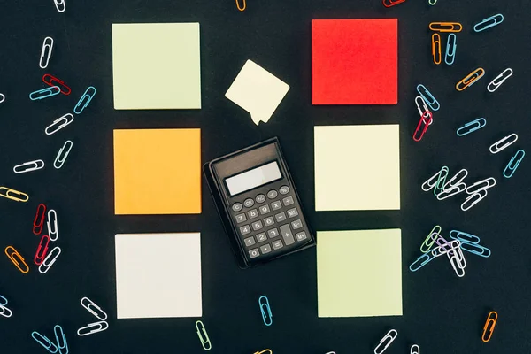 Вид сверху калькулятора, цветные скрепки и пустые заметки на черном — стоковое фото
