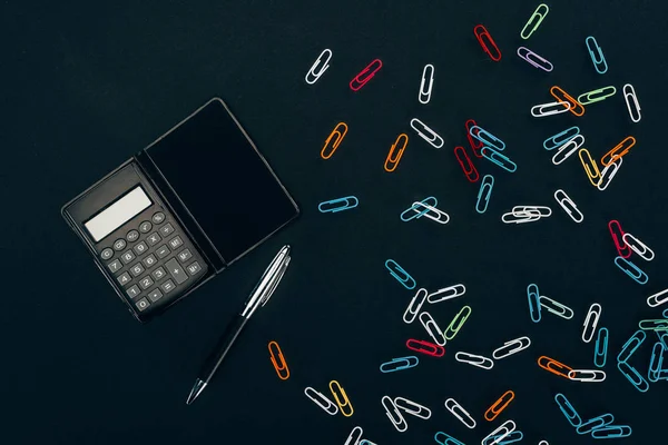 Top view of calculator, pen and colorful paper clips on black — Stock Photo