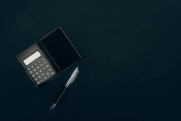 Top view of calculator and pen on black background — Stock Photo