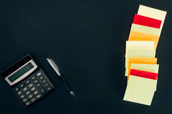 Top view of various colorful blank notes, calculator and pen on black — Stock Photo