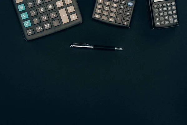 Top view of three calculators of different sizes and pen on black — Stock Photo