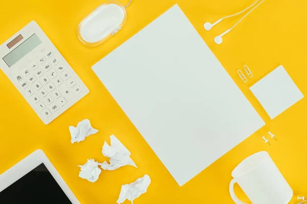 Top view of blank sheet of paper, crumpled papers, notes, calculator, earphones, computer mouse and digital tablet isolated on yellow — Stock Photo