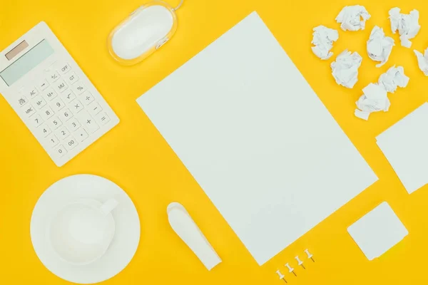 Vista superior de la hoja de papel en blanco, papeles arrugados, notas, calculadora y ratón de ordenador aislados en amarillo - foto de stock