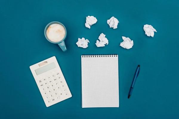 Top view of blank notebook with pen, calculator and crumpled papers on blue — Stock Photo