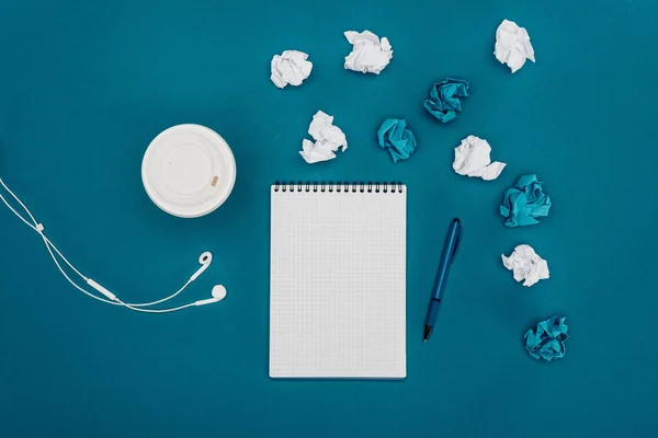 Vista superior de notebook em branco com caneta, papéis amassados e café para ir com fones de ouvido em azul — Fotografia de Stock